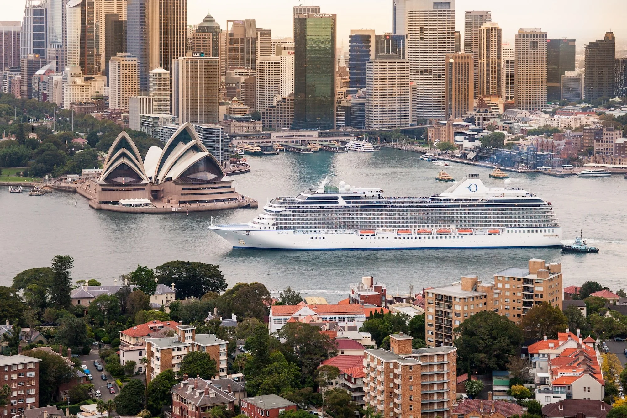 A city skyline with tall buildings, including the Sydney Opera House and a large cruise ship in the harbor.