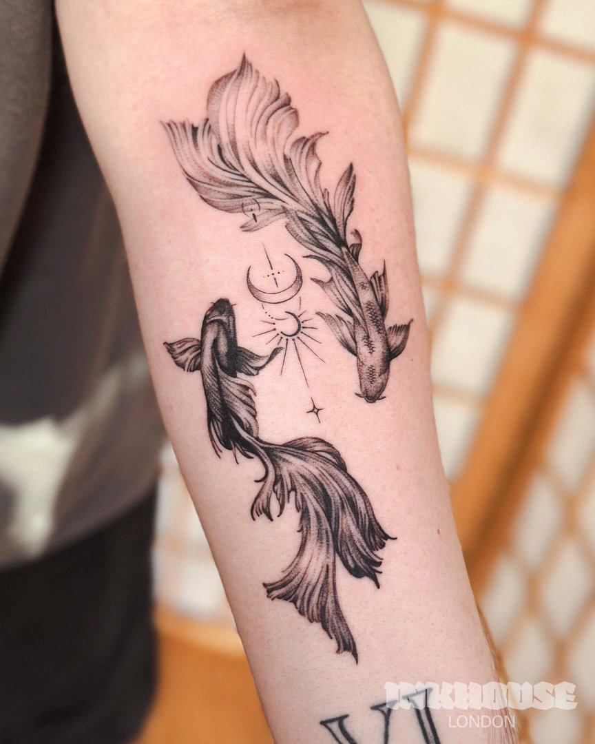 Tattoo on forearm of two koi fish with flowing tails, surrounded by crescent moons and small stars.