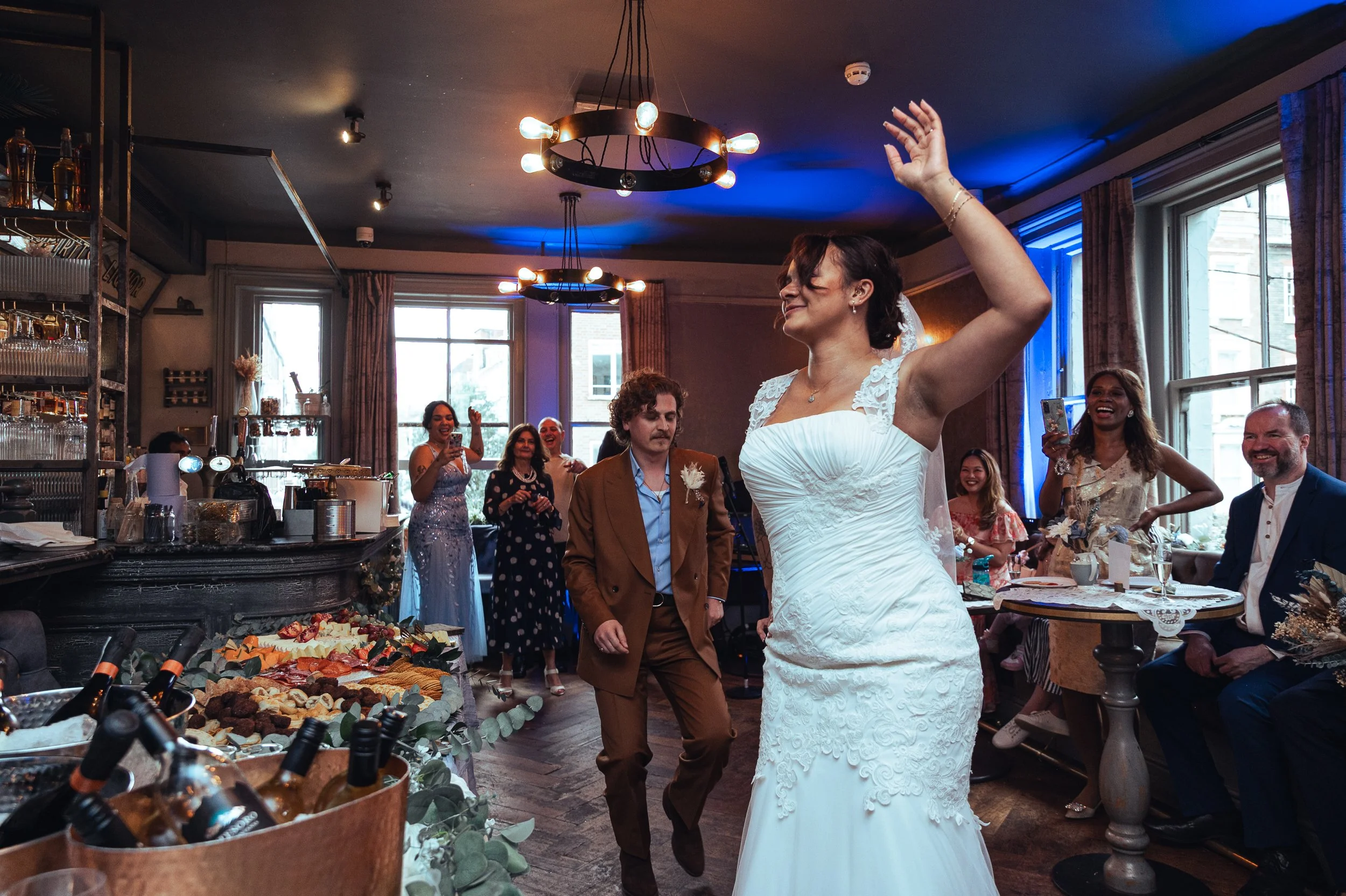 A bride dancing confidently at her wedding reception with guests clapping and smiling around her.