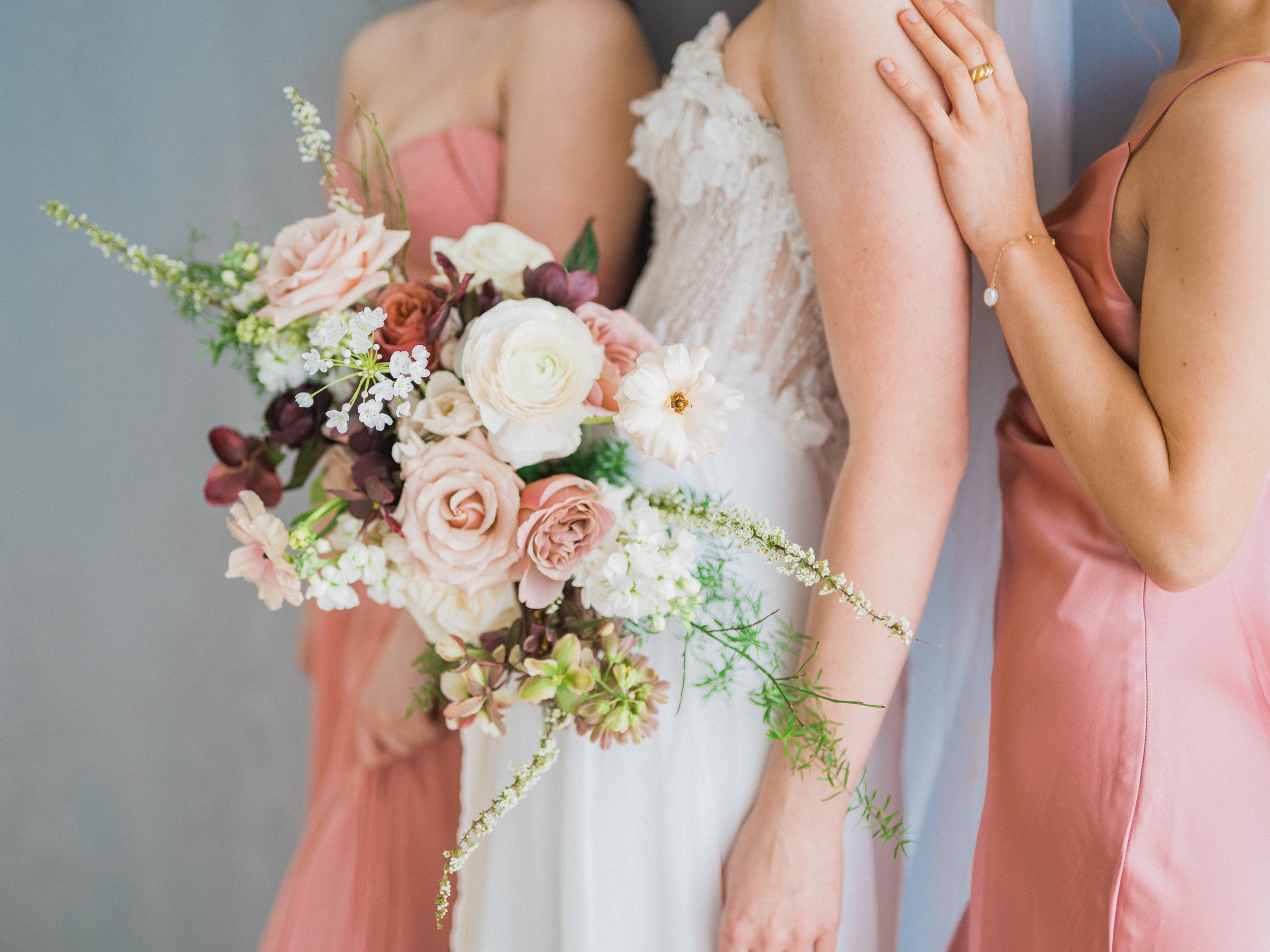 A bridesmaid in a pink dress and a bride holding romantic bridal bouquets designed by Twig & Bloom who offers wedding flowers in Regina and across Canada.