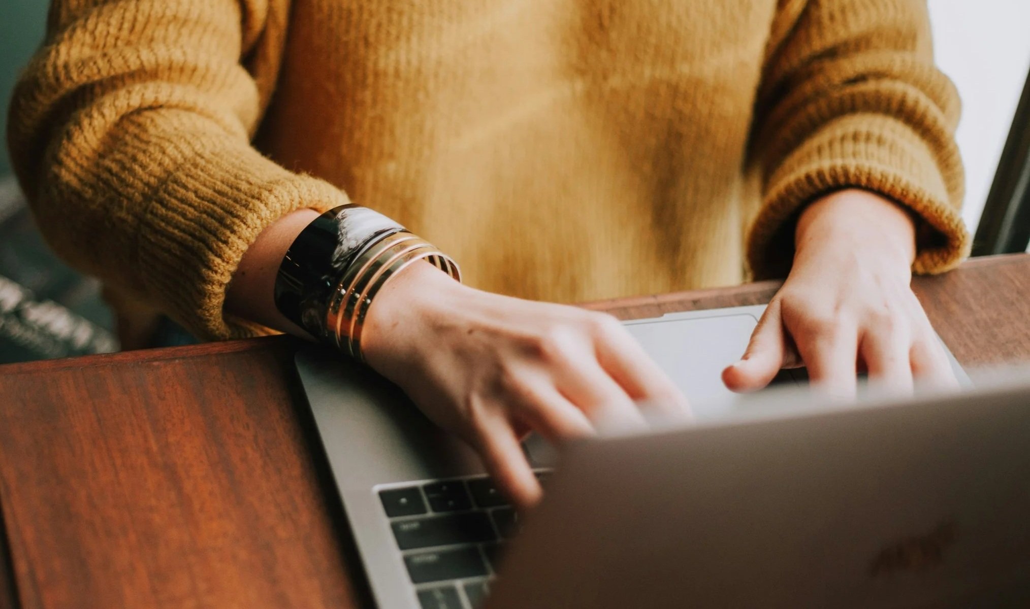 Photo of a person in a mustard yellow sweater's hands typing on a laptop