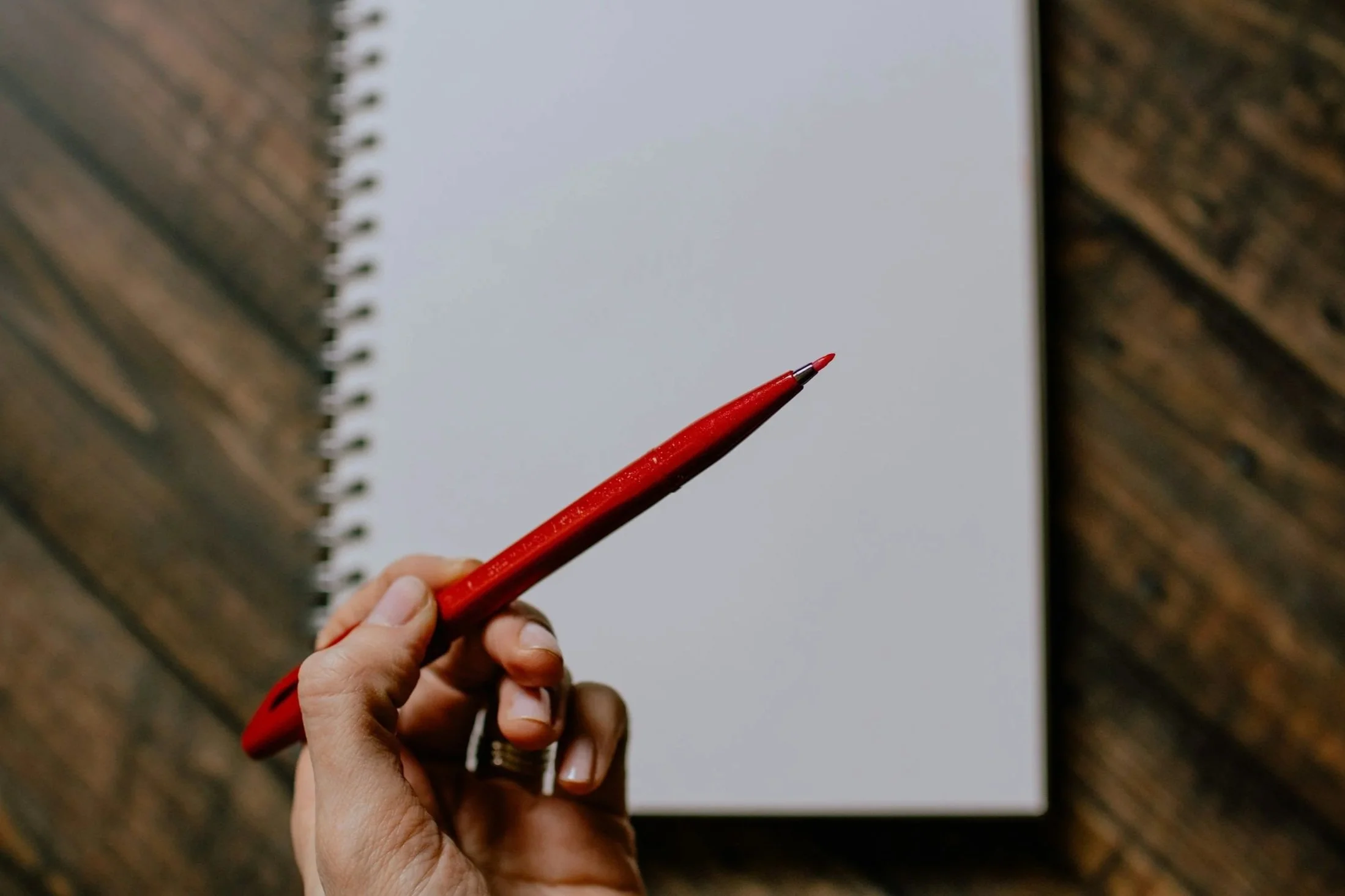 Phone of someone holding a red pen over a blank notebook