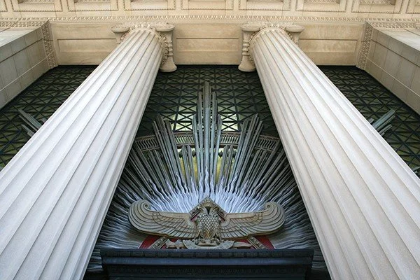 Majestic entrance of a classical building with large columns, ornate carvings, and a decorative eagle relief above the doorway.