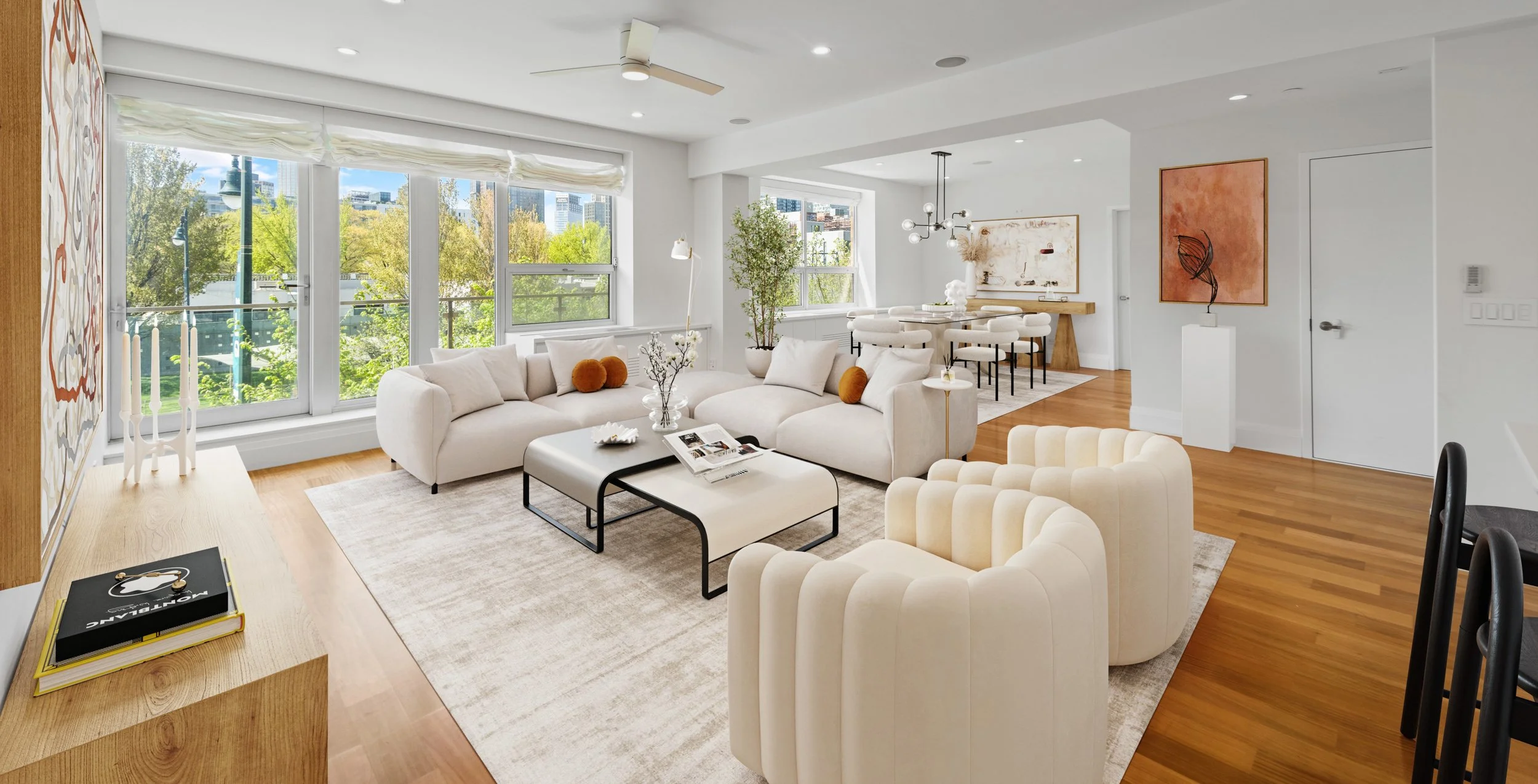 Bright, modern living room with large windows, white sofas, cream armchairs, wooden floors, and minimalist decor.