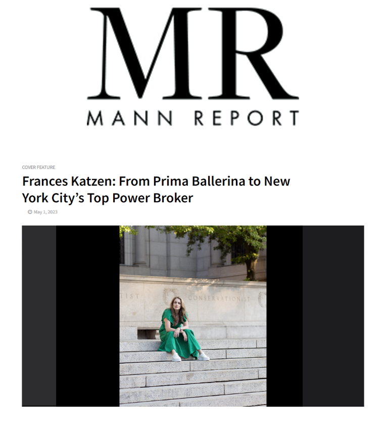 A young woman in a green dress sitting on stone steps outside in daylight, next to a tree and a stone building.