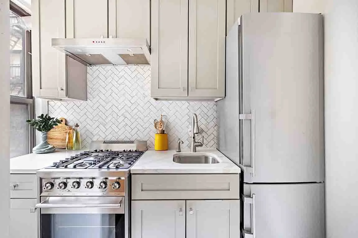 White kitchen with gray cabinets, a silver refrigerator, a stove, a sink, and a white tile backsplash.
