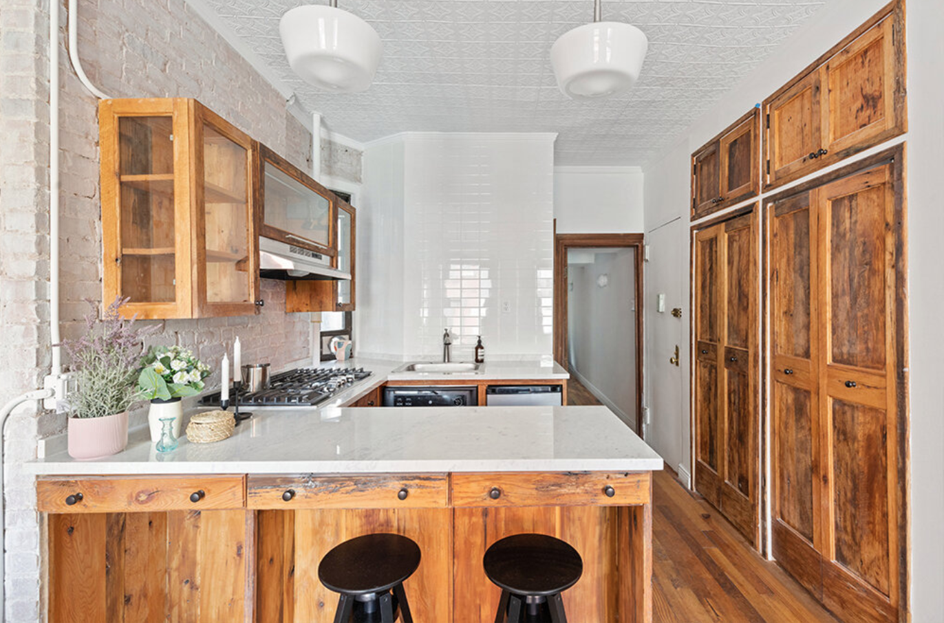 Kitchen with wooden cabinets, white countertop, brick and tile walls, and hardwood flooring.