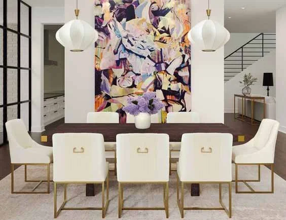 Modern dining room with a dark wood table, six white upholstered chairs, two hanging white pendant lights, a large colorful abstract painting on the wall, and a vase with purple flowers on the table.