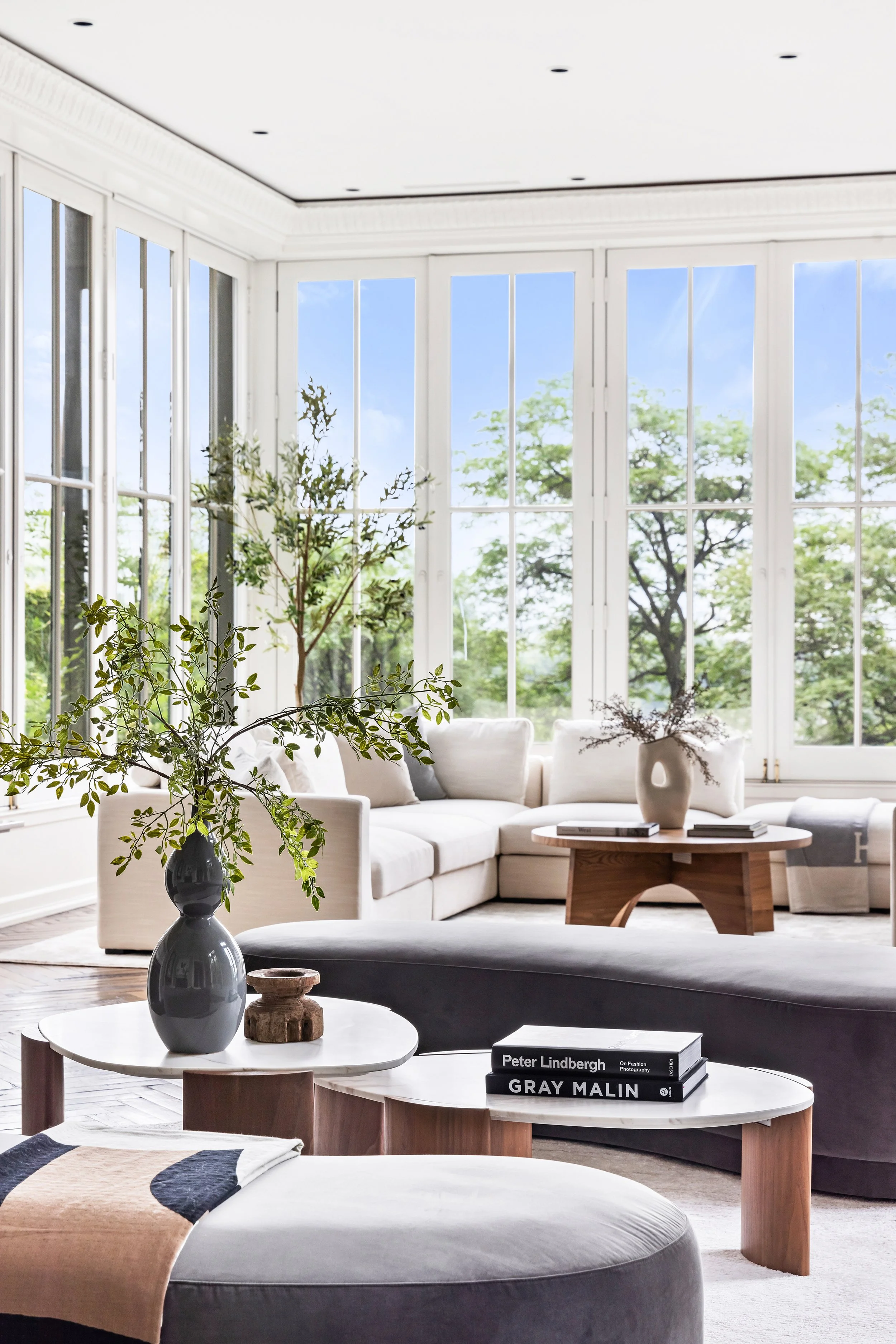 Bright living room with large windows, white sofa, wooden coffee table, and potted plants.
