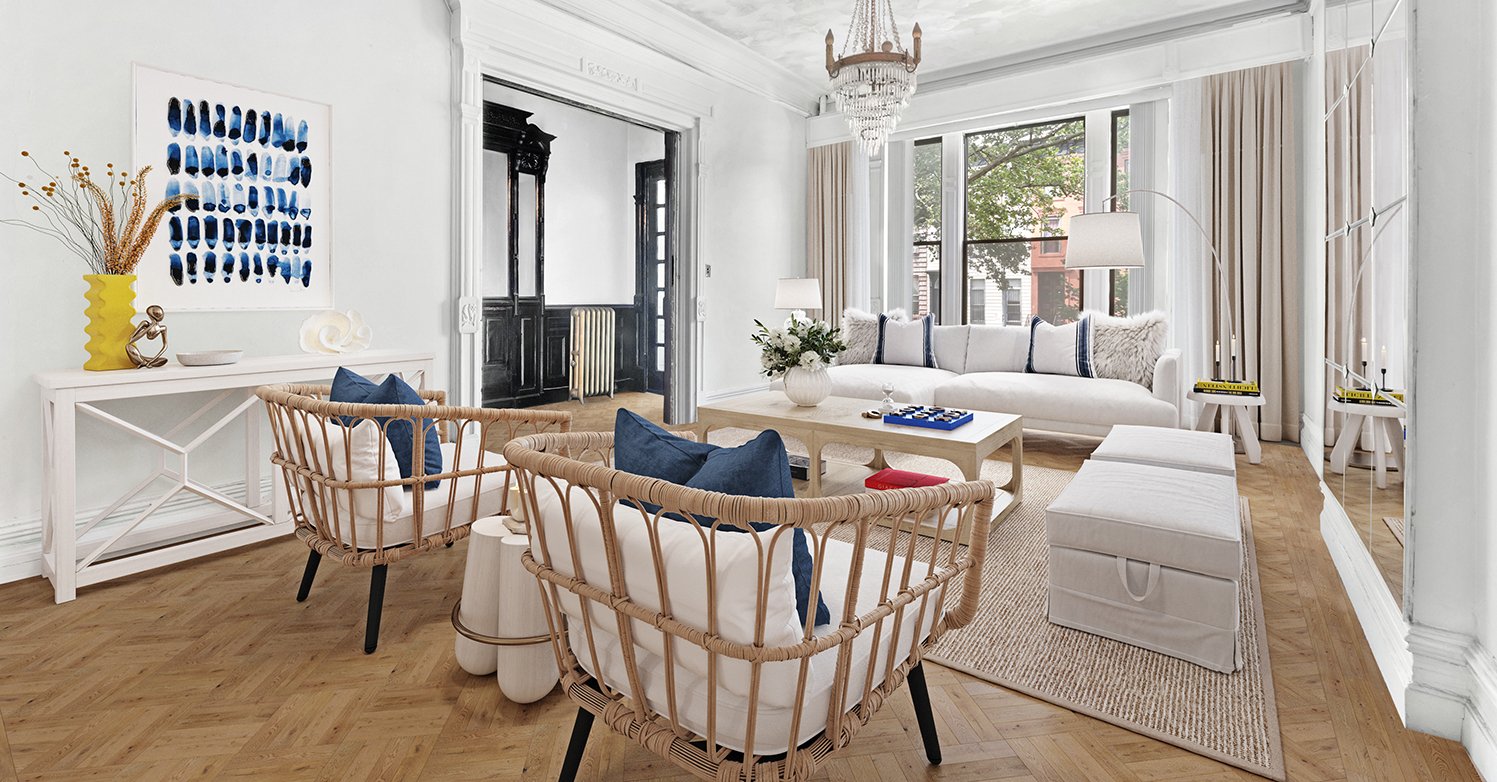 Bright living room with white walls, large windows, white sofa, woven armchairs with blue cushions, glass coffee table, a large abstract blue painting on the wall, chandelier, and beige curtains.
