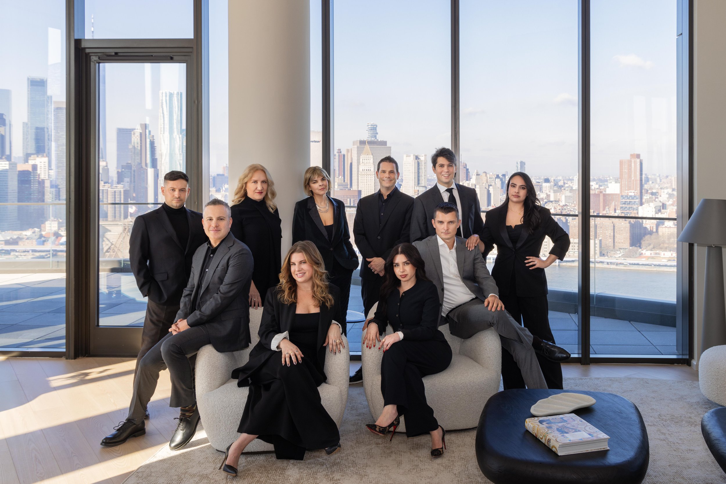 A diverse group of ten professionally dressed individuals posing in a modern high-rise office with large windows and a city skyline view.