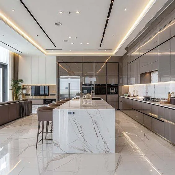 Modern kitchen with marble island, sleek gray cabinetry, built-in appliances, and a sitting area with stools and a sofa.