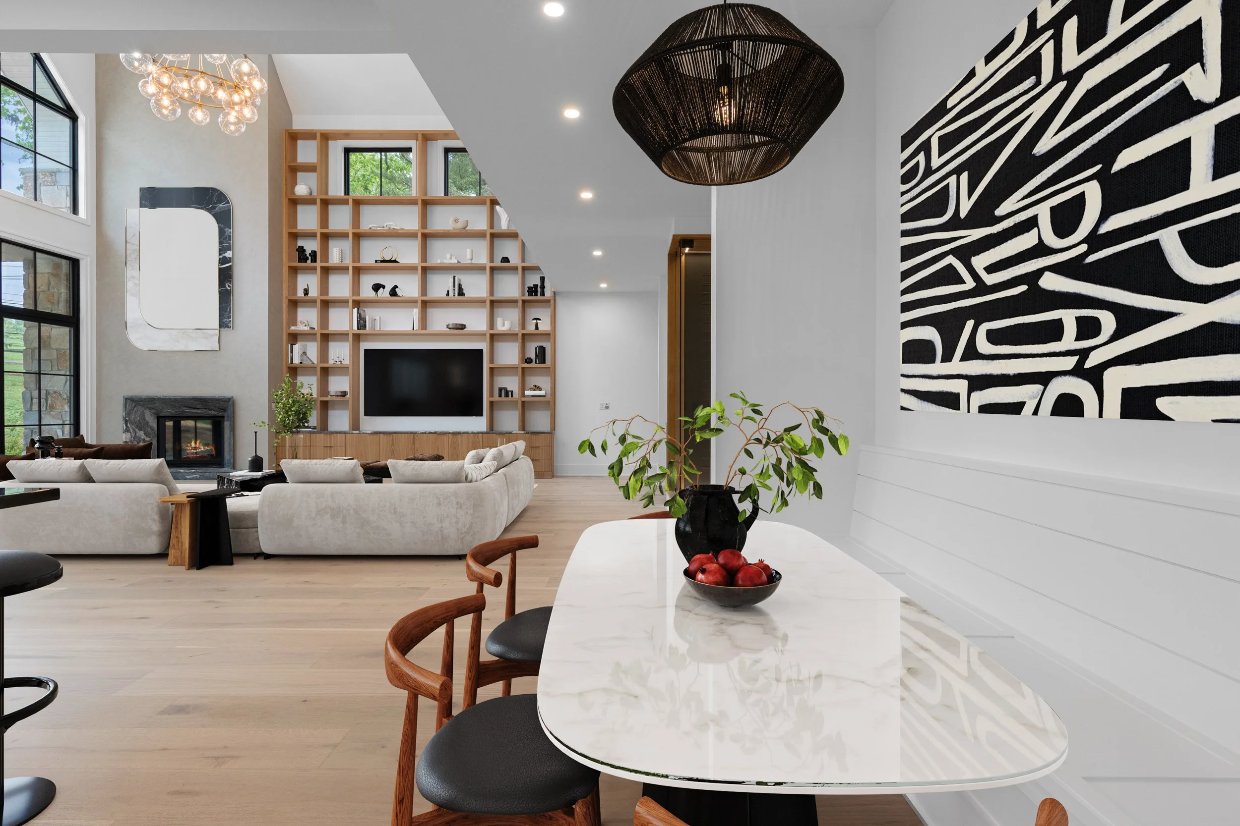 Modern living room with beige sofas, a wood-paneled entertainment wall with a TVand open shelving filled with decor. Large windows let in natural light, and a unique black chandelier hangs from the ceiling. Adjacent to the living room is a white dini