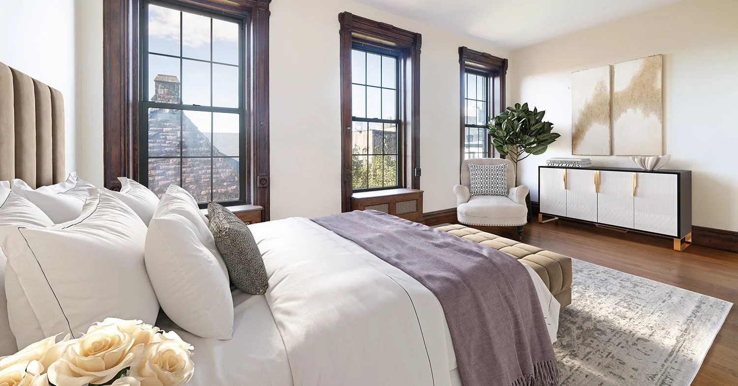 Bright bedroom with three large windows, a white bed with multiple pillows, a beige bench at the foot of the bed, a white armchair, a green potted plant, a modern white and black dresser, and abstract wall art.