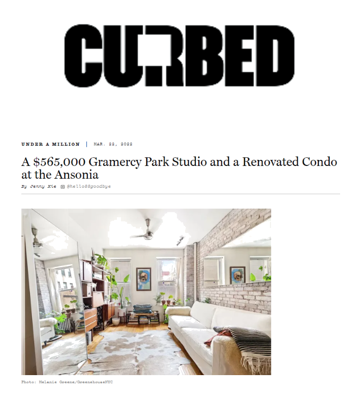 Modern living room with white sofa, brick accent wall, large mirror, and large windows with plants and artwork.