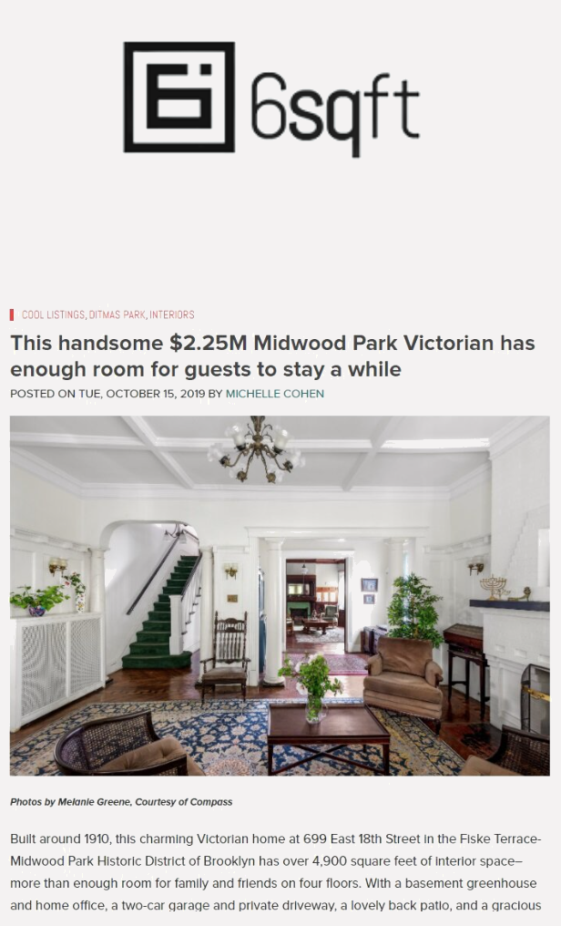 An interior view of a spacious Victorian-style living room with high ceilings, a chandelier, white walls, and dark wood floors. The room is furnished with armchairs, a wooden coffee table, and various decorative plants.