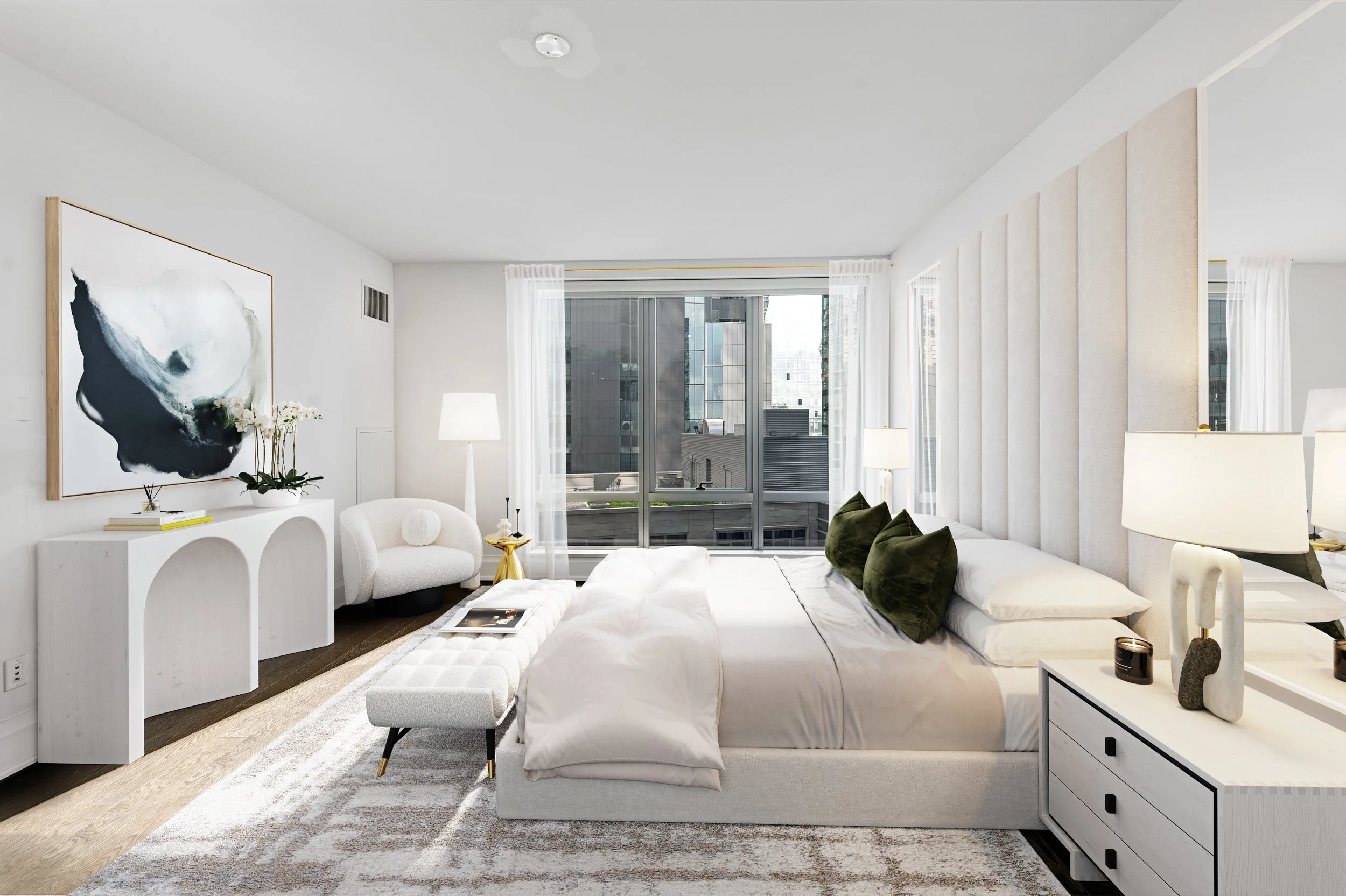 A modern, bright bedroom with white walls, large window, white bed with green pillows, a white bench at the foot of the bed, and a white dresser with decorative items. There is a white armchair, a white side table with a lamp, and abstract artwork on the wall.