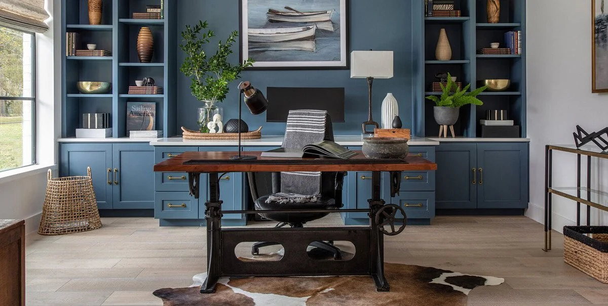 Home office with a wooden desk, black office chair, blue built-in shelves, and a cowhide rug.
