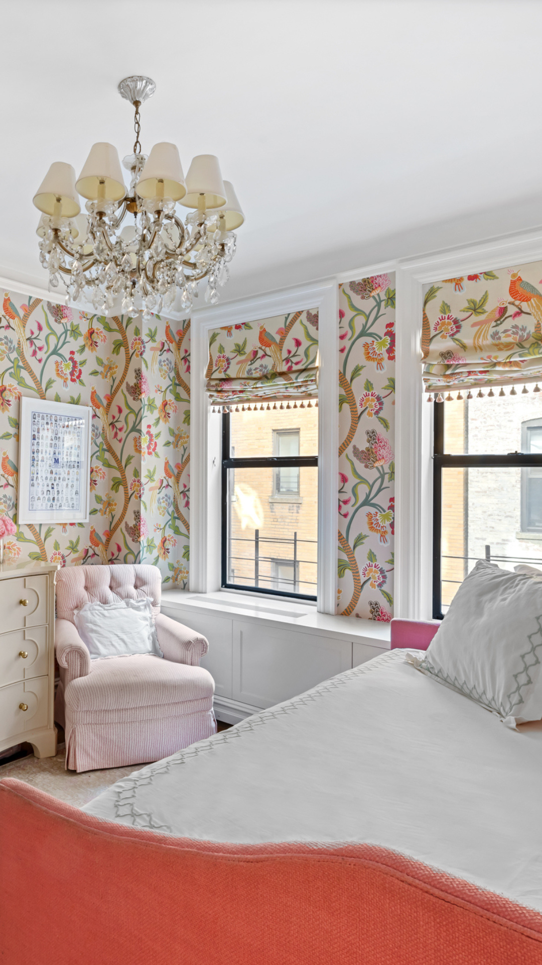 Colorful bedroom with floral/ bird wallpaper, chandellier, and coral and white daybed with a pink recliner in the corner