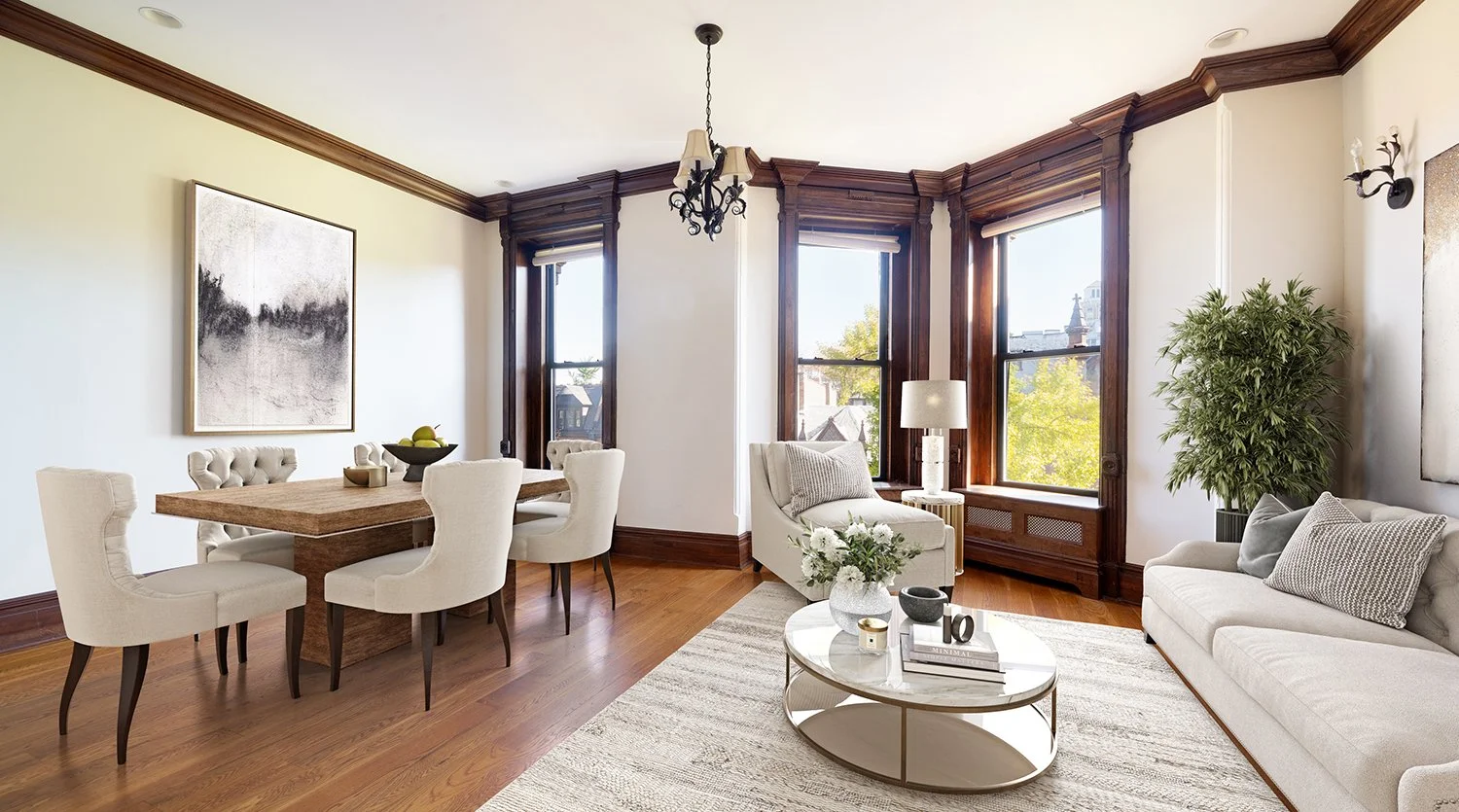 Living room with a dining area, large windows with wood trim, white sofas, a round coffee table with books and decor, and a large potted plant.