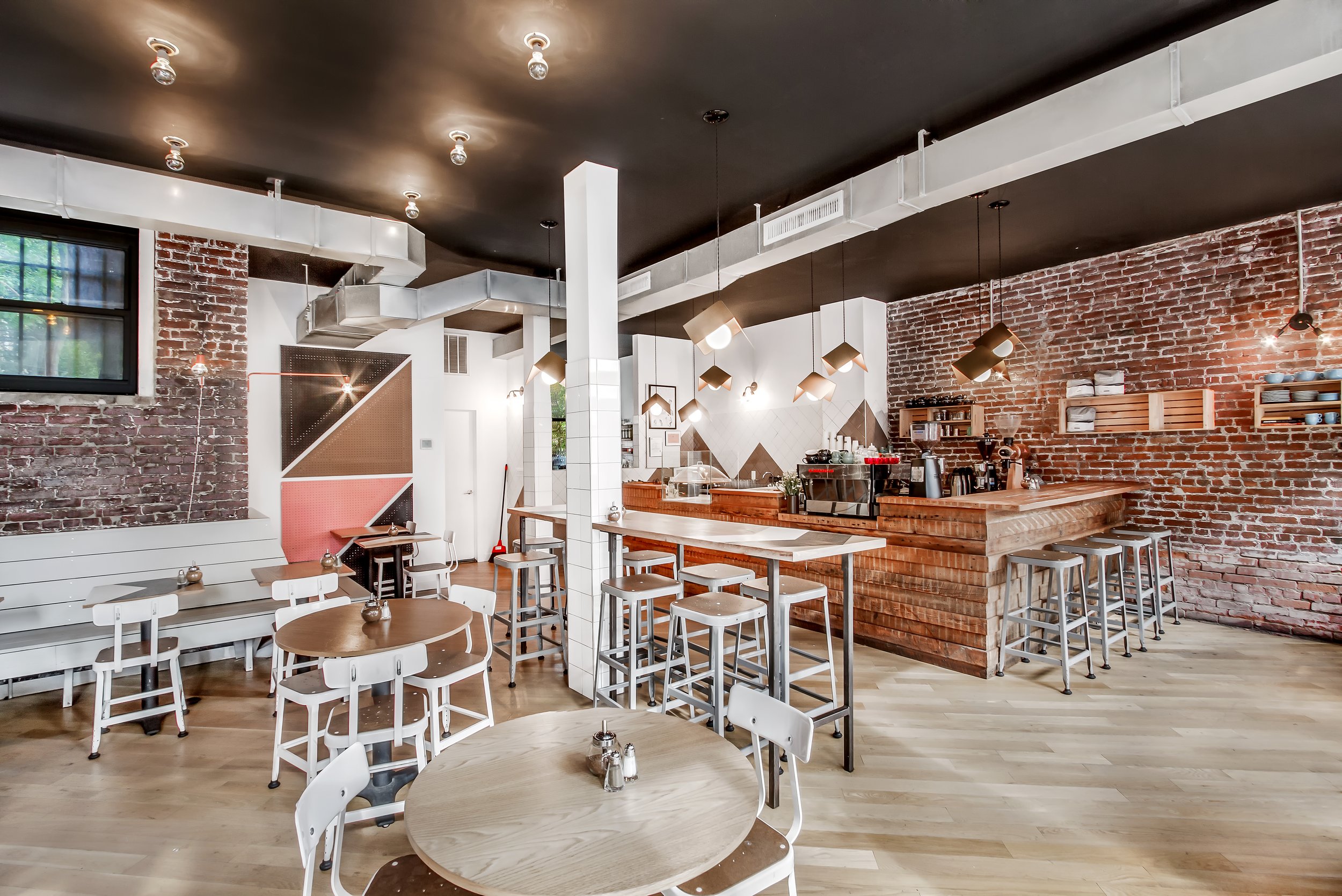 Interior of a modern cafe with brick walls, wooden furniture, and hanging pendant lights.