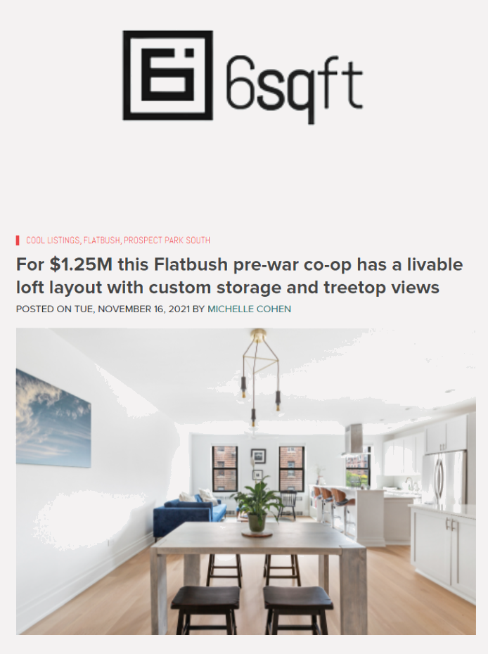 Modern, open-concept kitchen and dining area with white cabinetry, large windows, a wooden dining table, and a living space with a blue sofa.