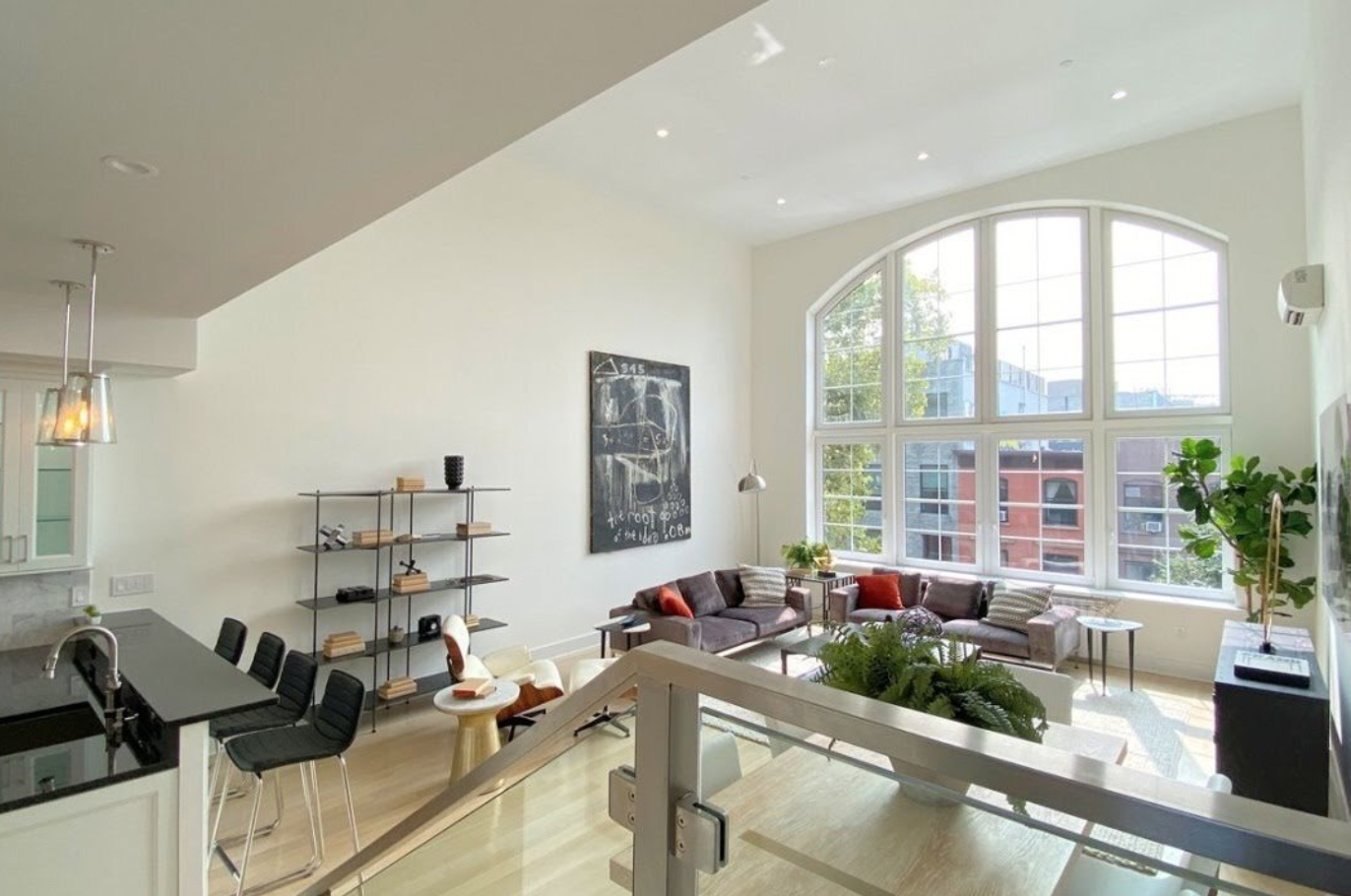 Modern living room with large arched window, sectional sofas, bookshelf, and decorative plants.
