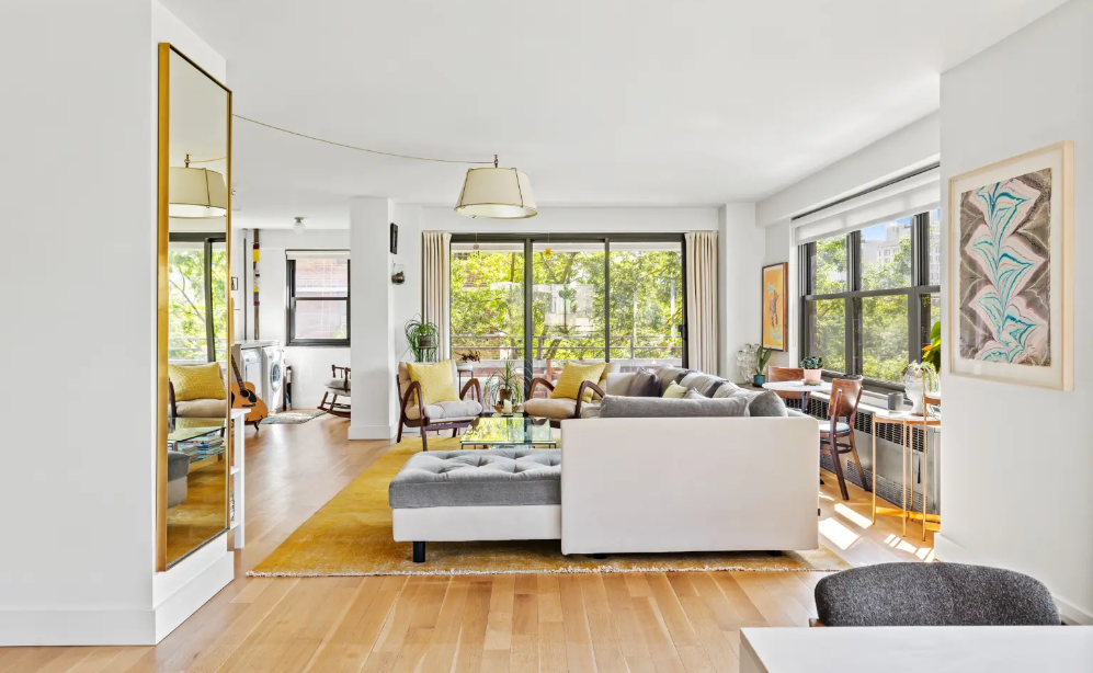 Bright living room with large windows, modern furniture, and artwork on the walls, decorated with yellow and gray accents.