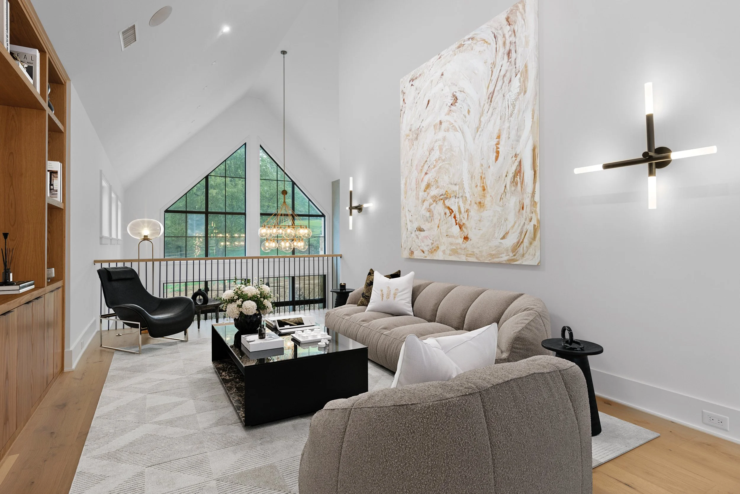 Modern living room with a large abstract painting on the wall, beige sofa, black coffee table, black lounge chair, and large geometric window with green trees outside.