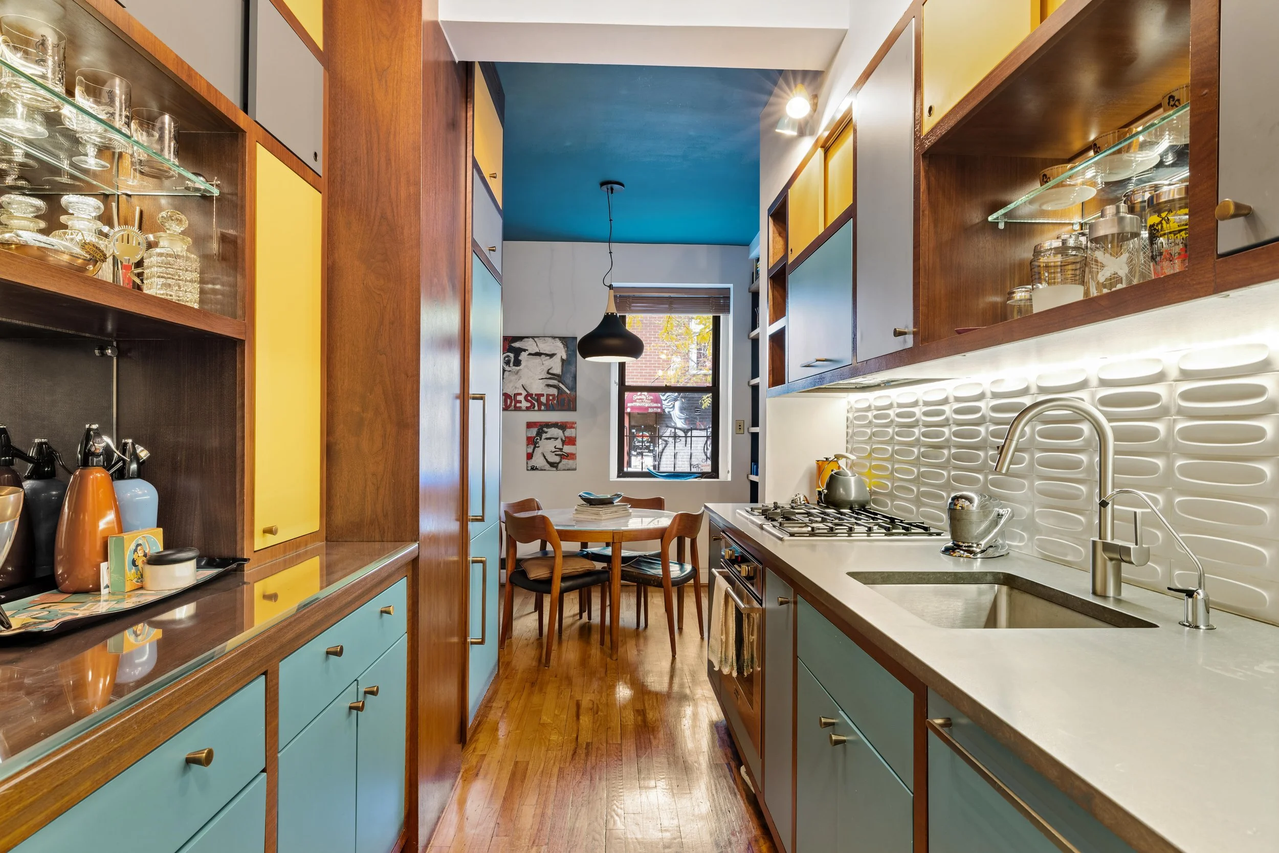 Colorful kitchen with yellow and blue cabinets, wooden accents, and a small dining table near a window.
