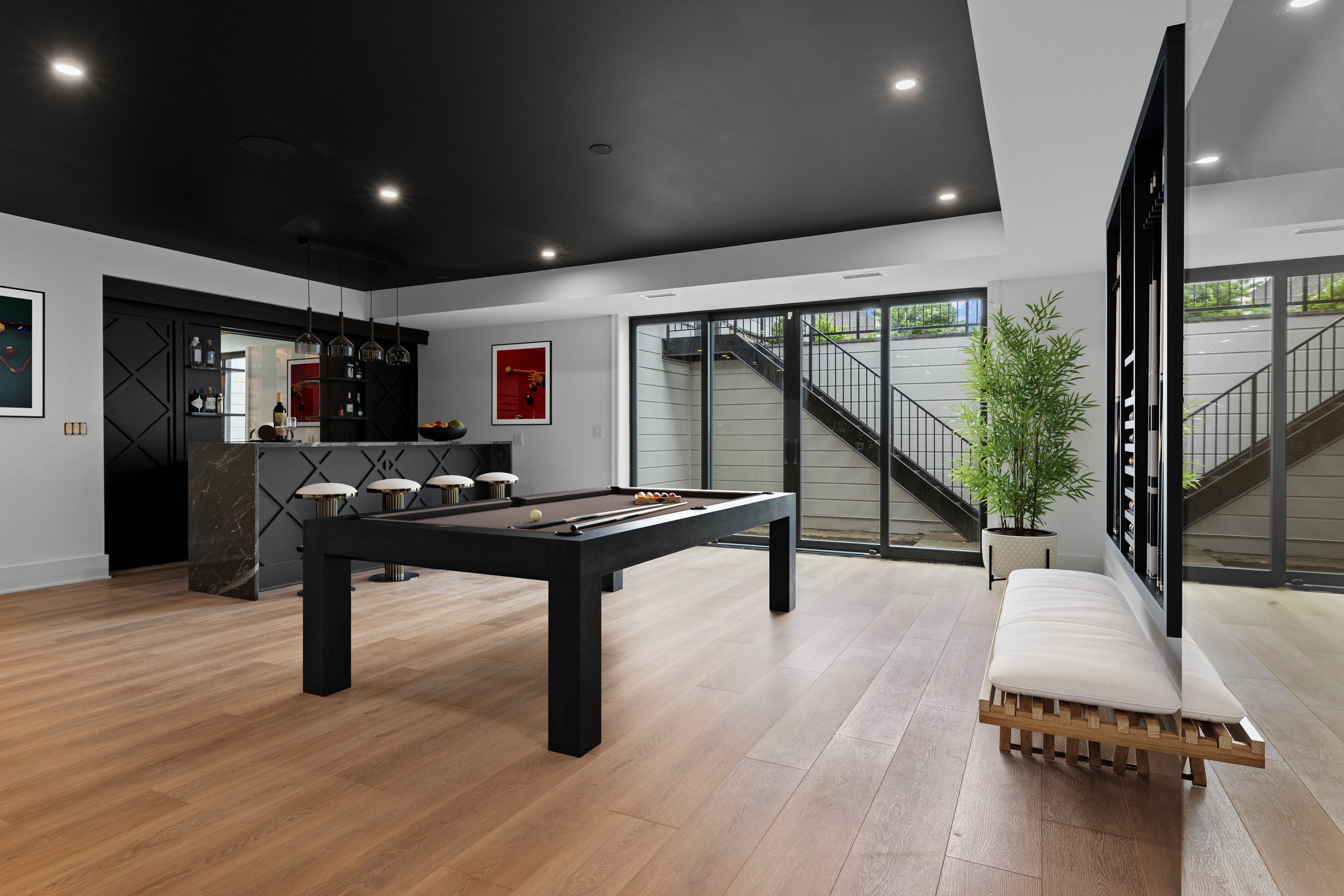 Modern game room with pool table, bar area with bar stools, large windows, and potted plant.