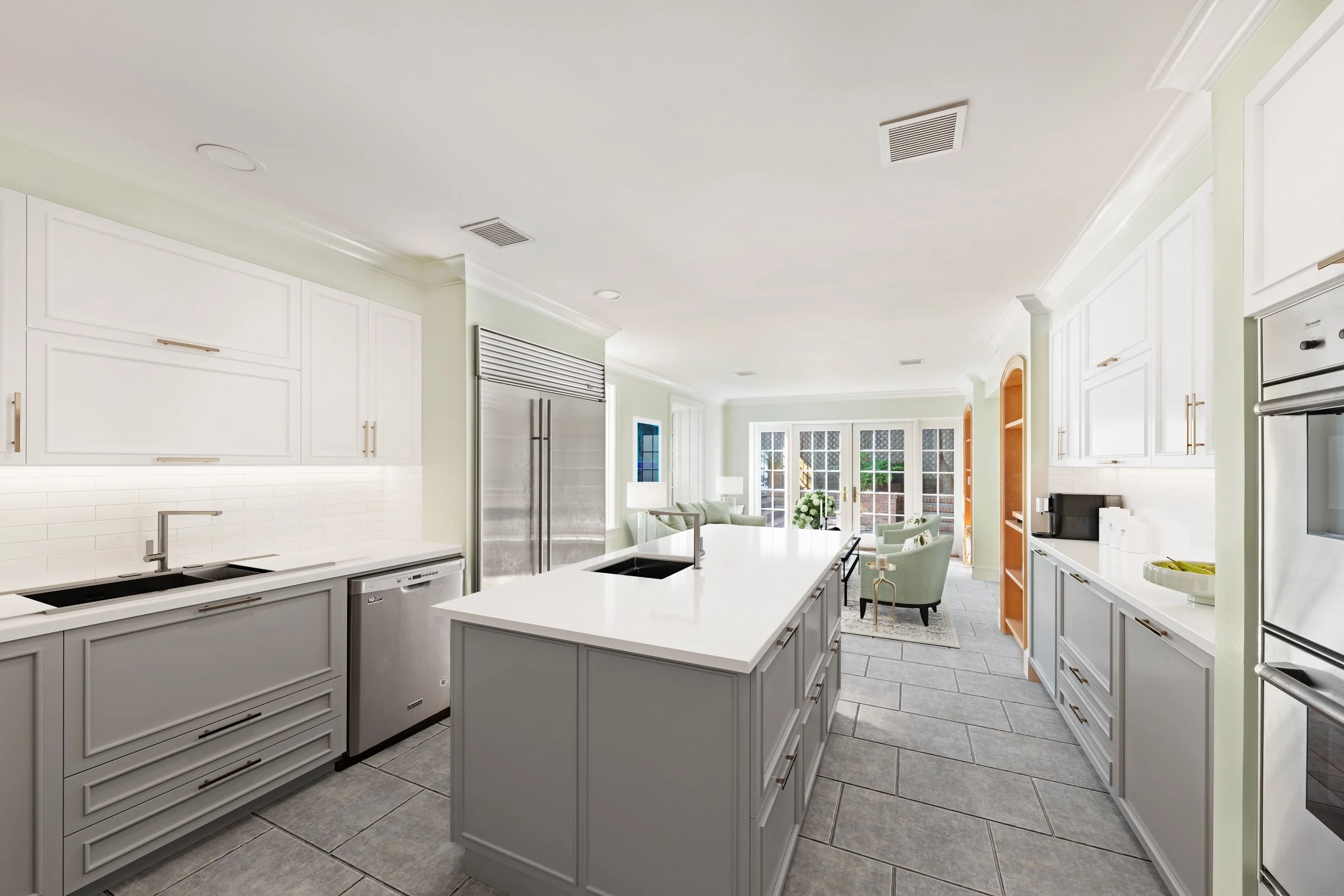 Bright, modern kitchen with white cabinets, a large central island, stainless steel appliances, and a seating area with chairs and a table near glass doors leading outside.