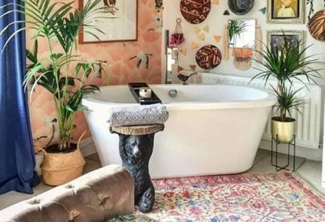 Modern bathroom with a freestanding bathtub, colorful wall art, potted plants, a rug, and a stool with a towel.