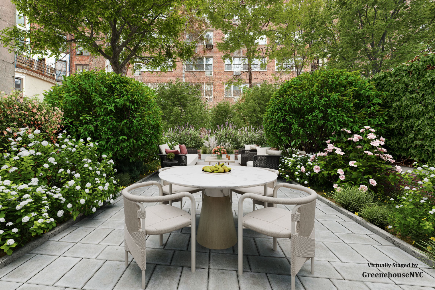 A lush outdoor garden patio with a white round table and four beige chairs in the foreground. Behind, there are black wicker sofas and armchairs with cushions, surrounded by green trees and blooming pink and white flowers. Tall apartment buildings are visible in the background.