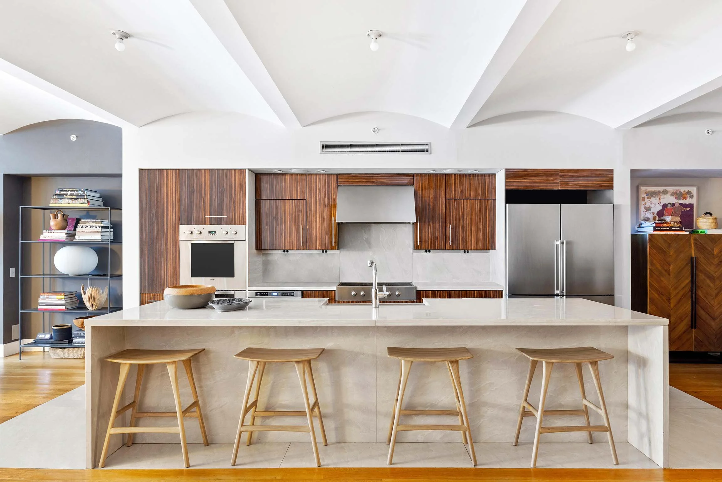 Modern kitchen with a white marble island, wooden cabinets, stainless steel appliances, and four wooden barstools.