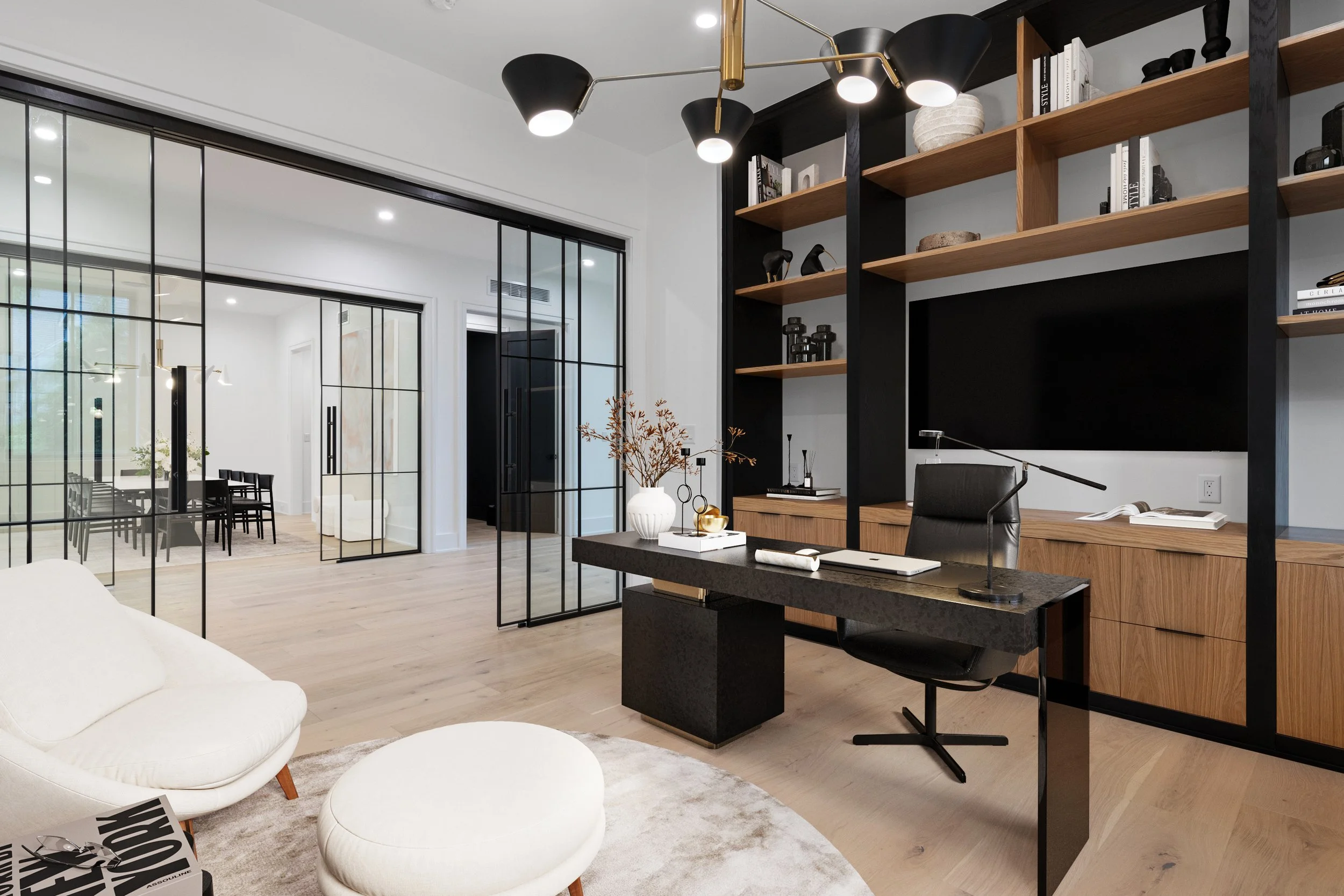 Modern home office with black and wood shelving, black desk, black office chair, white furniture, wood flooring, and sliding glass doors leading to a dining area.