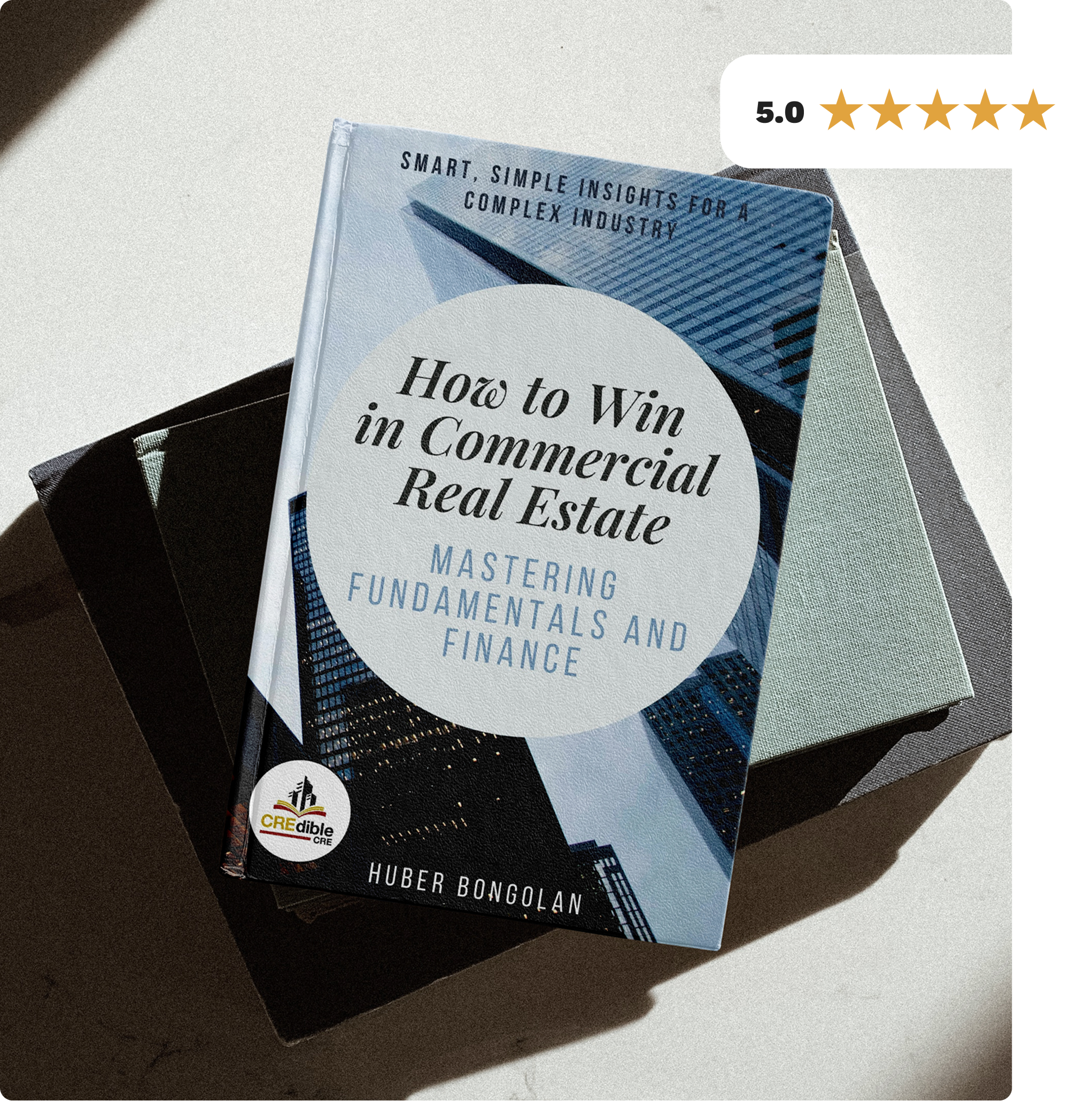 A book titled 'How to Win in Commercial Real Estate: Mastering Fundamentals and Finance' by Huber Bongolan, placed on a black box with a white background. The cover features city skyscraper images and a Crestible logo, with a 5-star review rating.