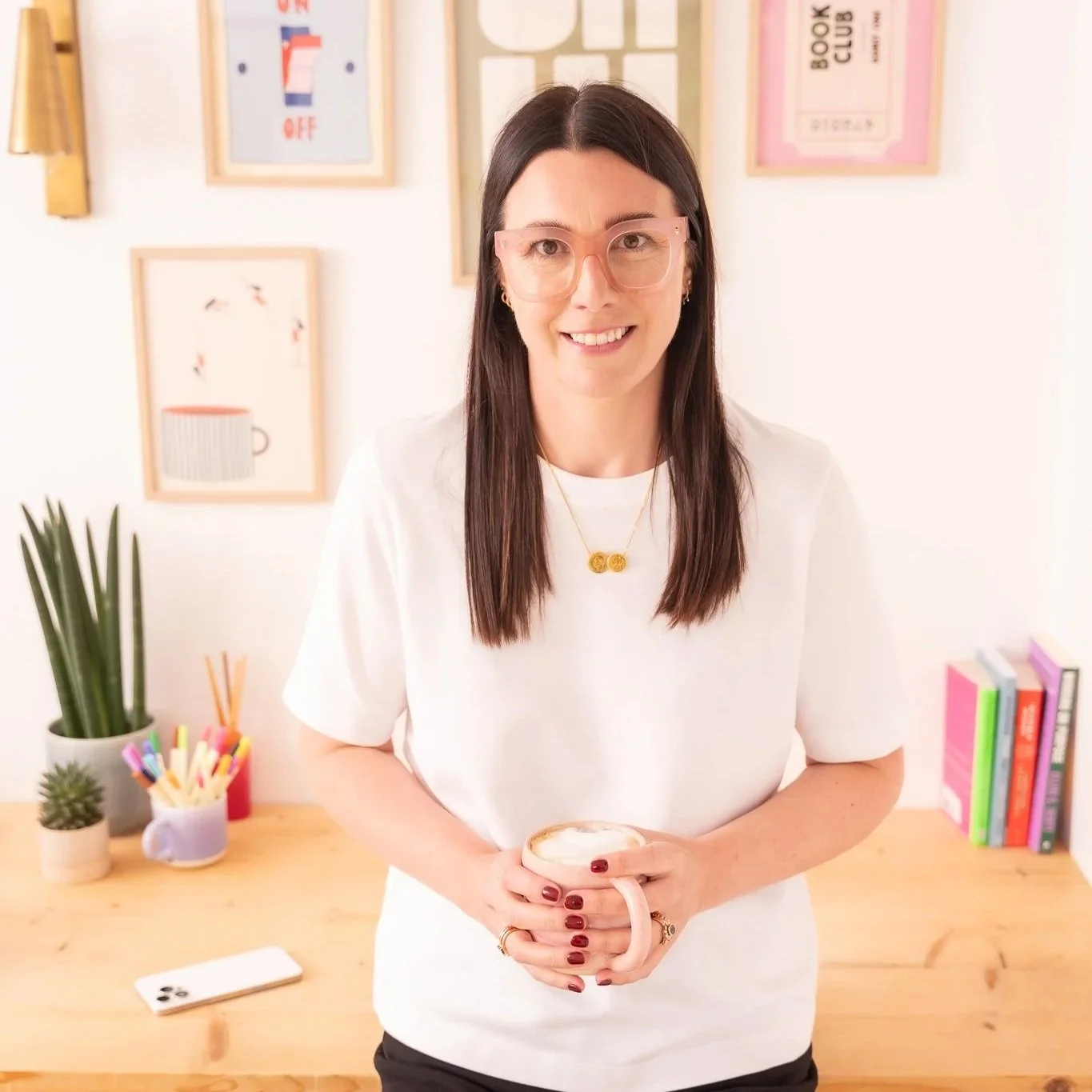 Harriet holding a pink mug of coffee in her colourful office