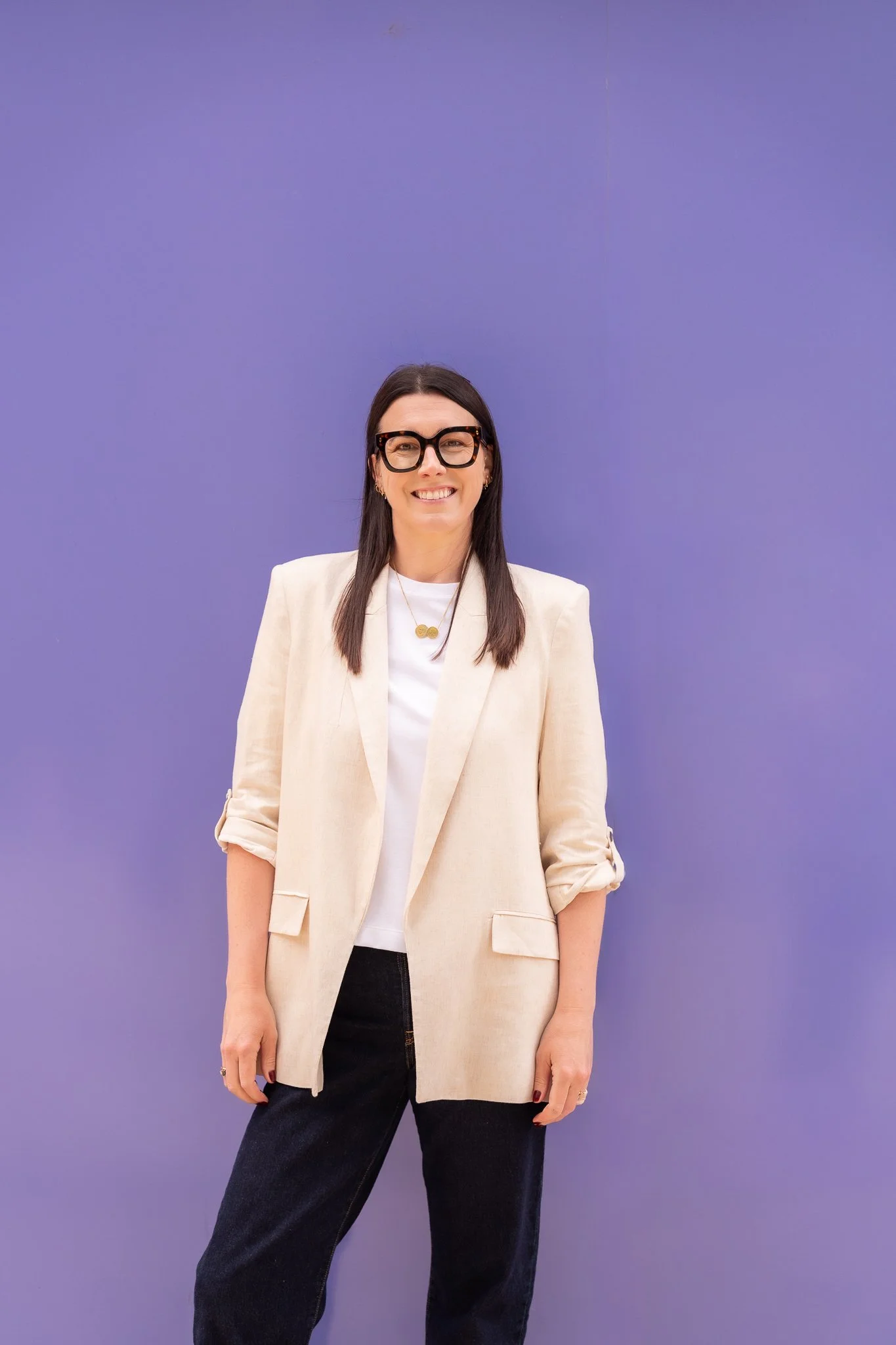 Harriet Cox smiling and stood in front of a lilac wall