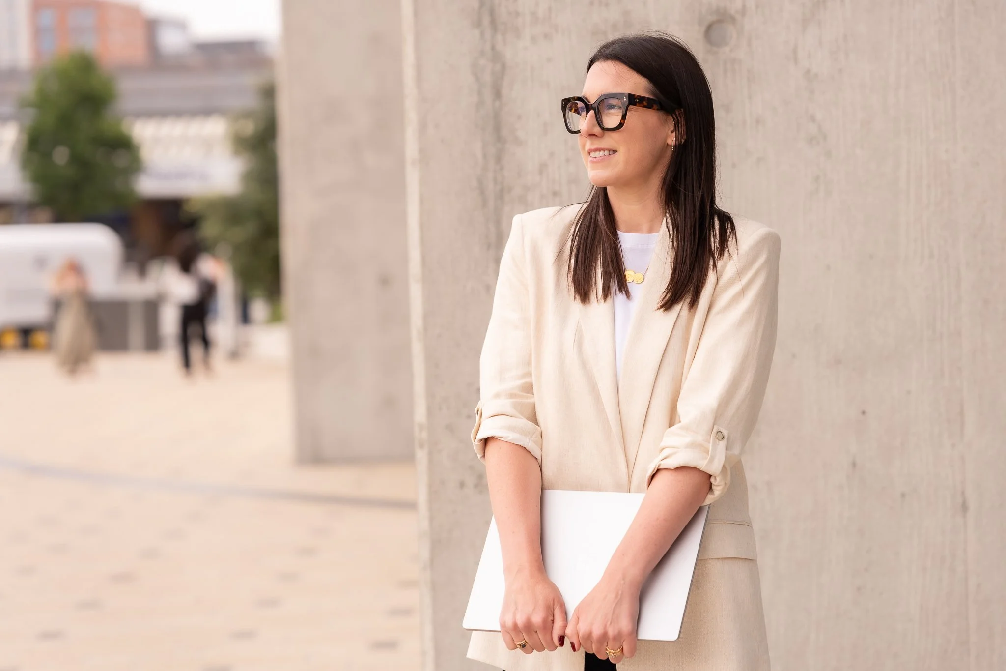 Harriet stood in an urban area in a cream jacket holding her laptop
