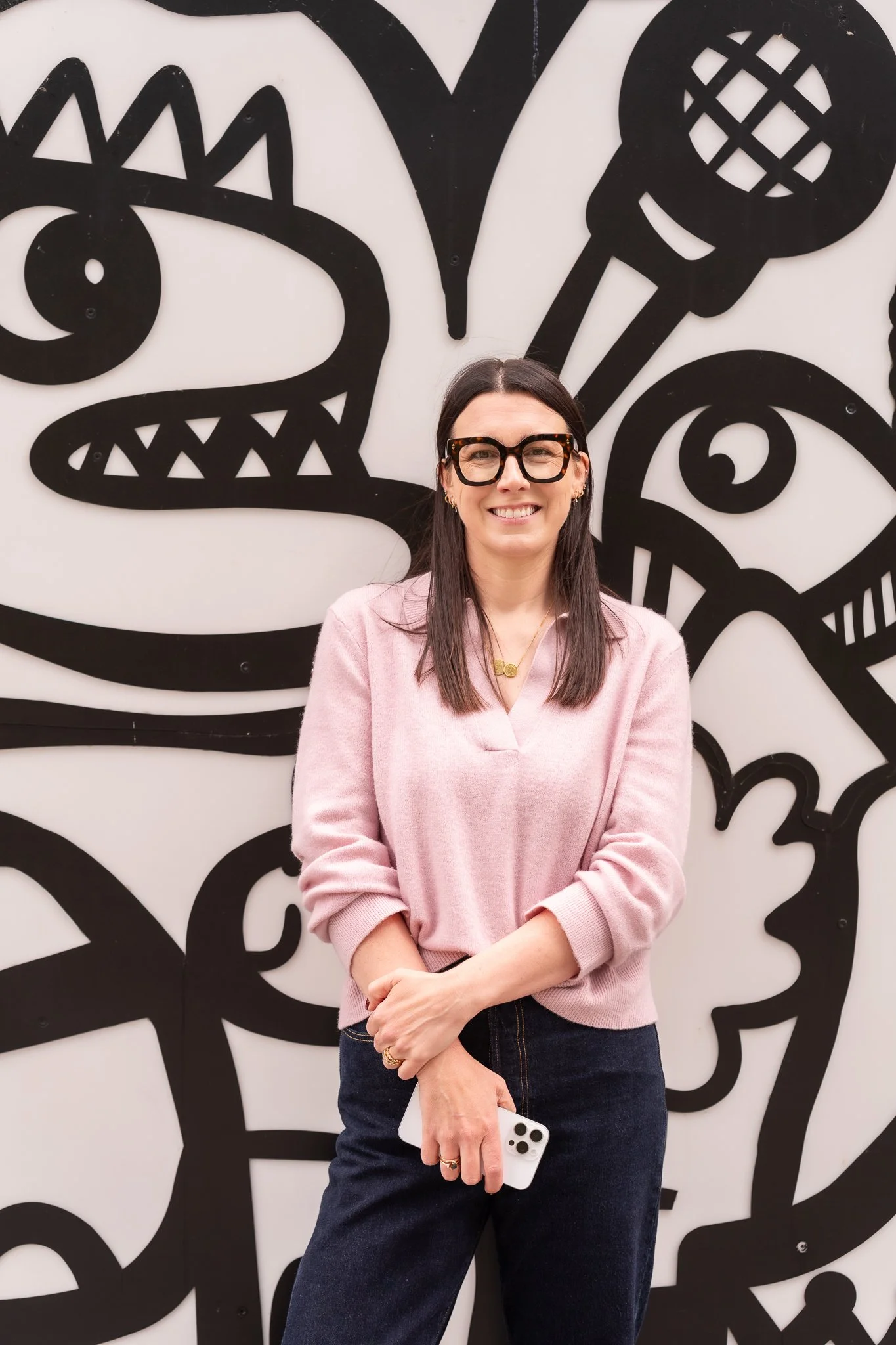 Harriet in a pink jumper against a black and white graffiti wall