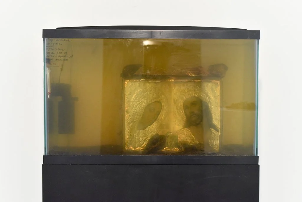 The Deterioration of Christ and His Servant Konstantinos Karagiannis. 30.5” x 12.5” x 67”. Fish tank, salt water,  icon, sand, rocks, thermometer, filter, tea light, pedestal. 2023
