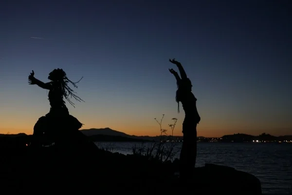 Silhouette of two people doing dance movements on a hill at sunset
