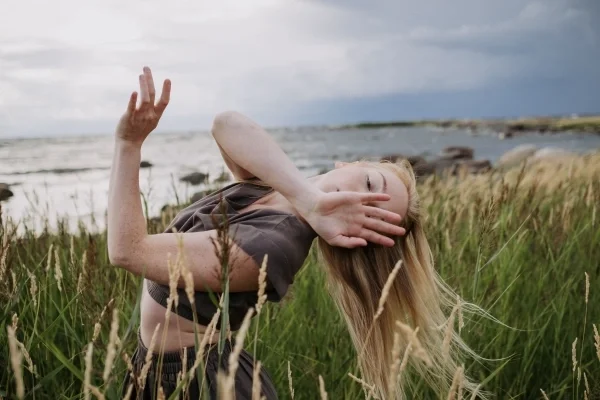 Girl doing hand and body motions in tall grass at the coast