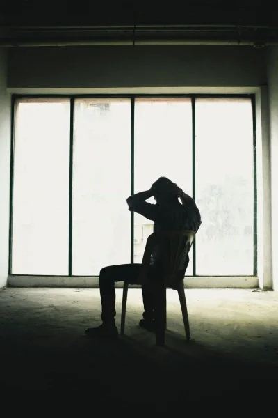 Silhouette of person sitting in chair with hands on head