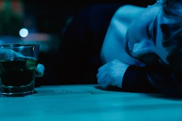 Person lying head in arm on a bar while holding glass