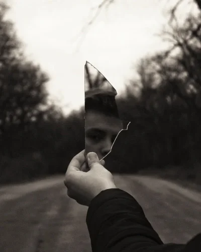 Black and white image of person holding shard or broken mirror