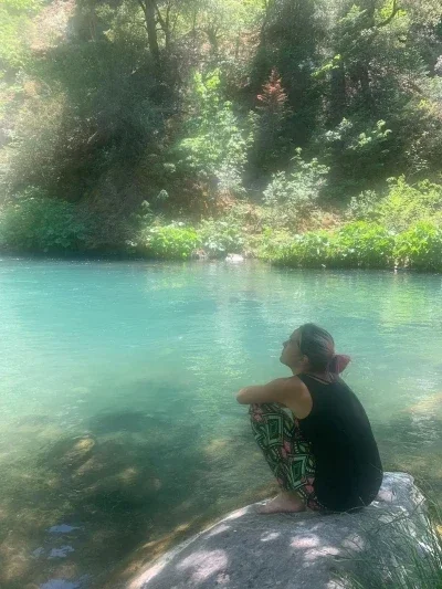 Woman crouching on rock by blue water pond