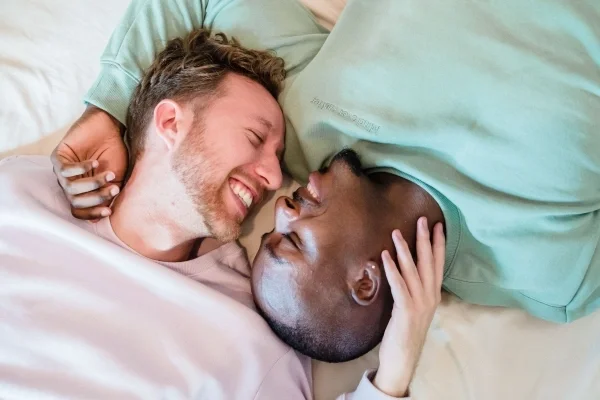 Two men lying on bed with faces very close smiling