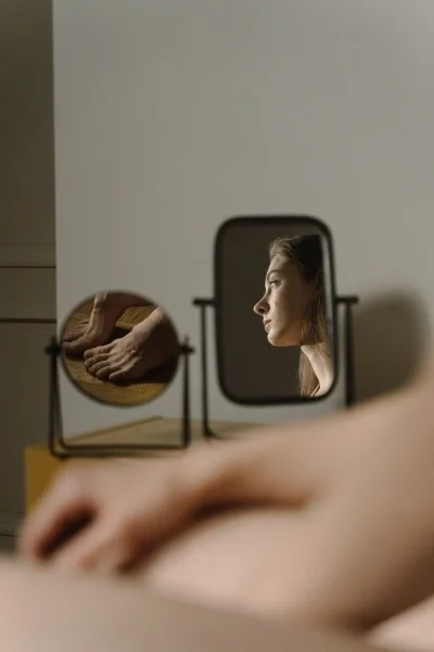 View of a woman sitting on bed as seen from two mirrors